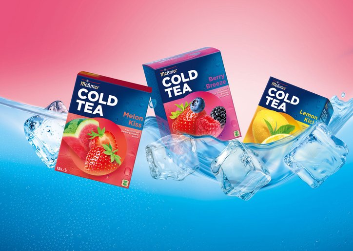 Drei Packungen Meßmer Cold Tea in den Sorten Melon Kiss, Berry Breeze und Lemon Kick schweben zwischen Eiswürfeln und spritzendem Wasser vor einem pink-blauen Hintergrund.